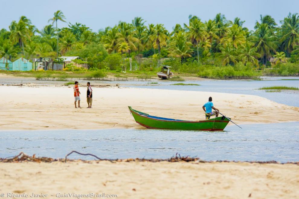 Imagem de pescador no barco e nativos na areia da Praia Corumbau.